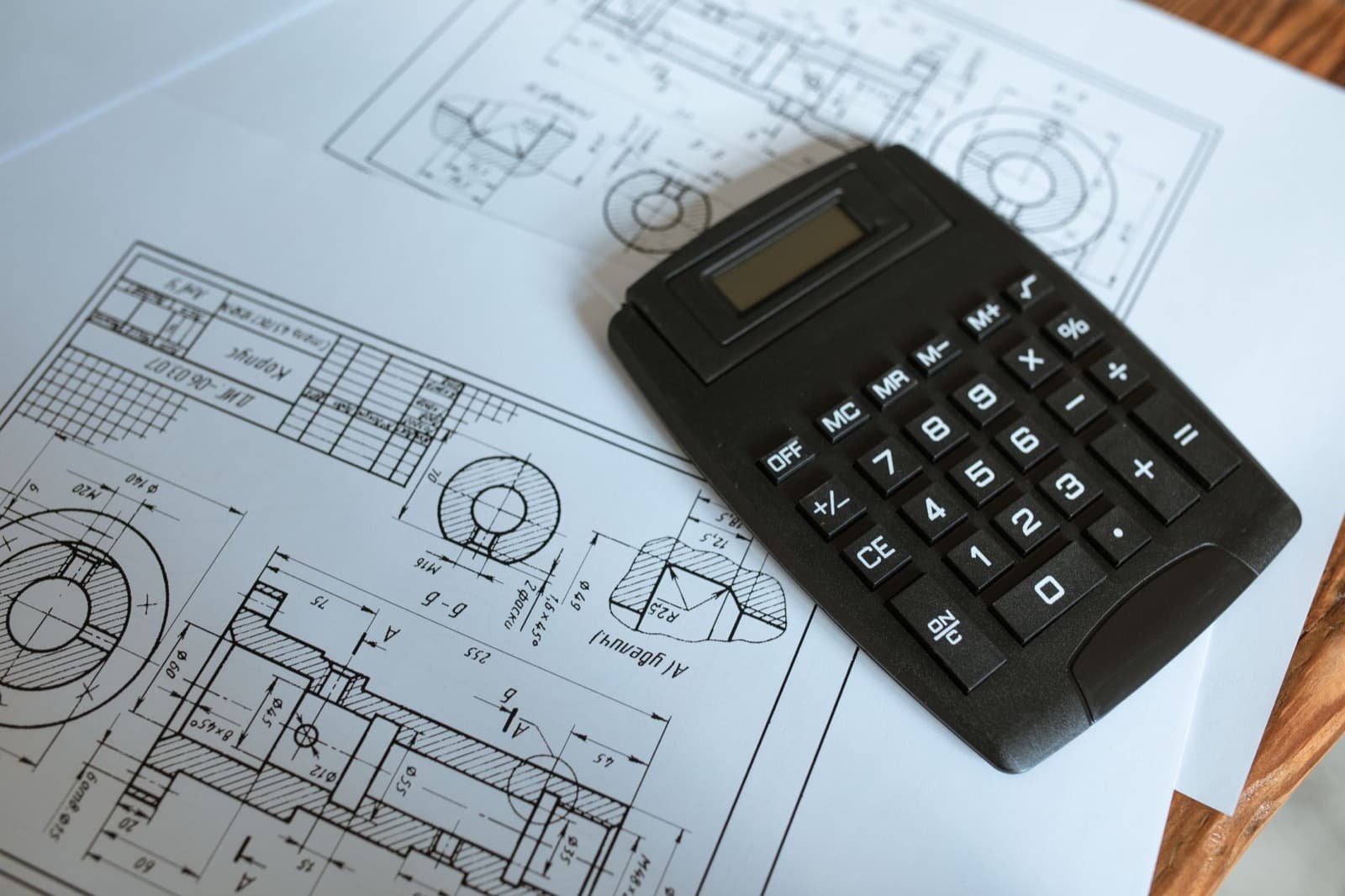 Black calculator resting on technical engineering drawings — budgeting elevator capital planning against the equipment specs