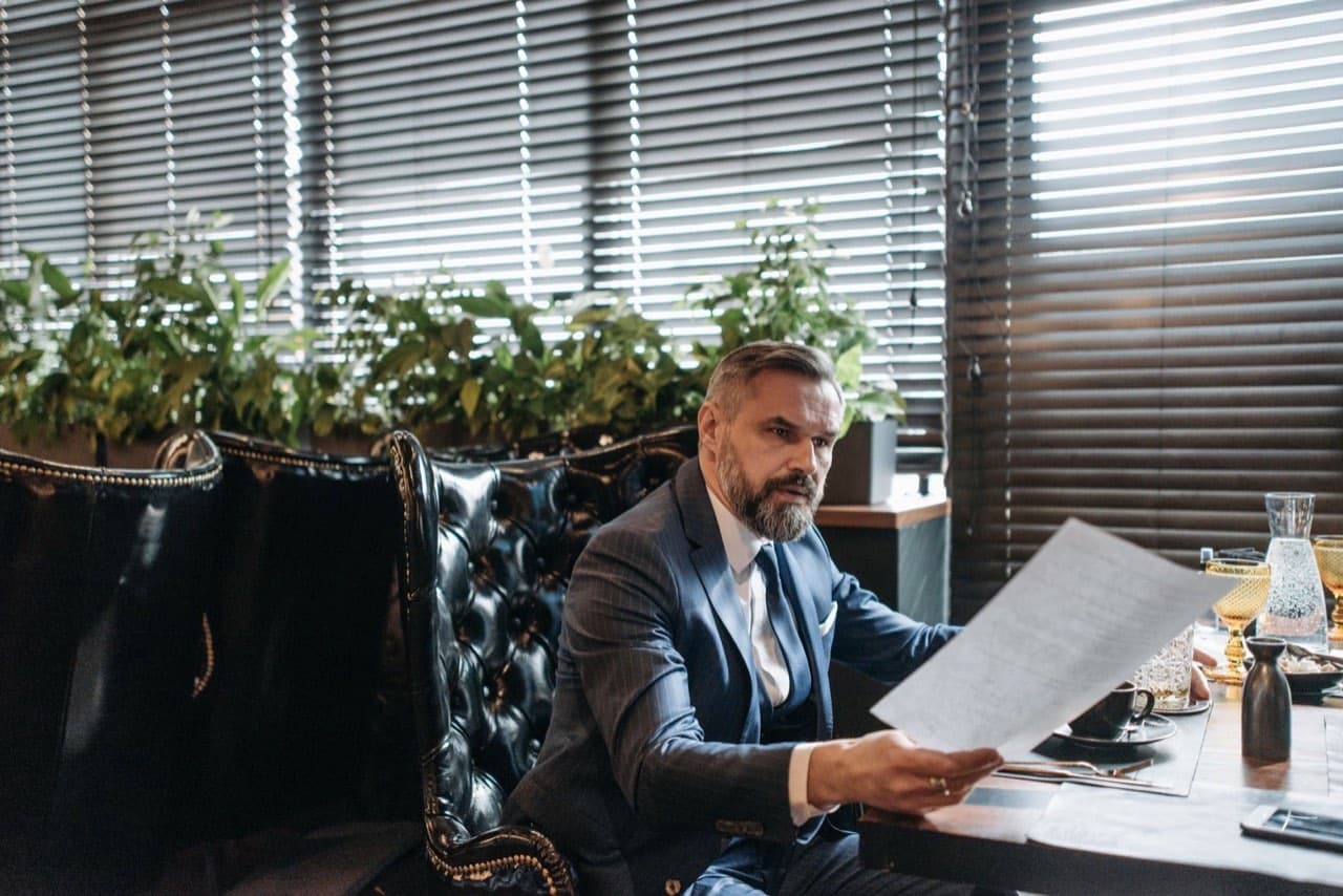 Businessman in a suit studying a printed proposal at his desk — deciding whether an elevator quote is fairly priced