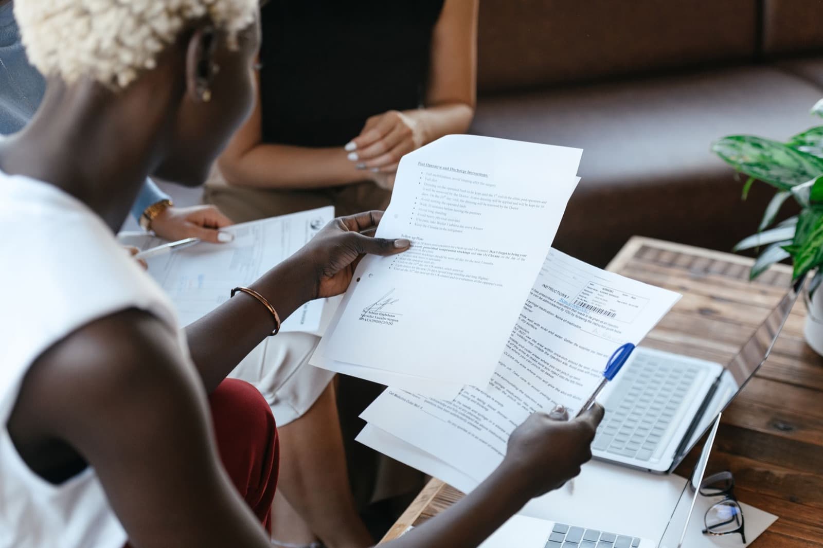 Two professionals holding printed documents side by side over a desk with a laptop — comparing competitive elevator bids line by line