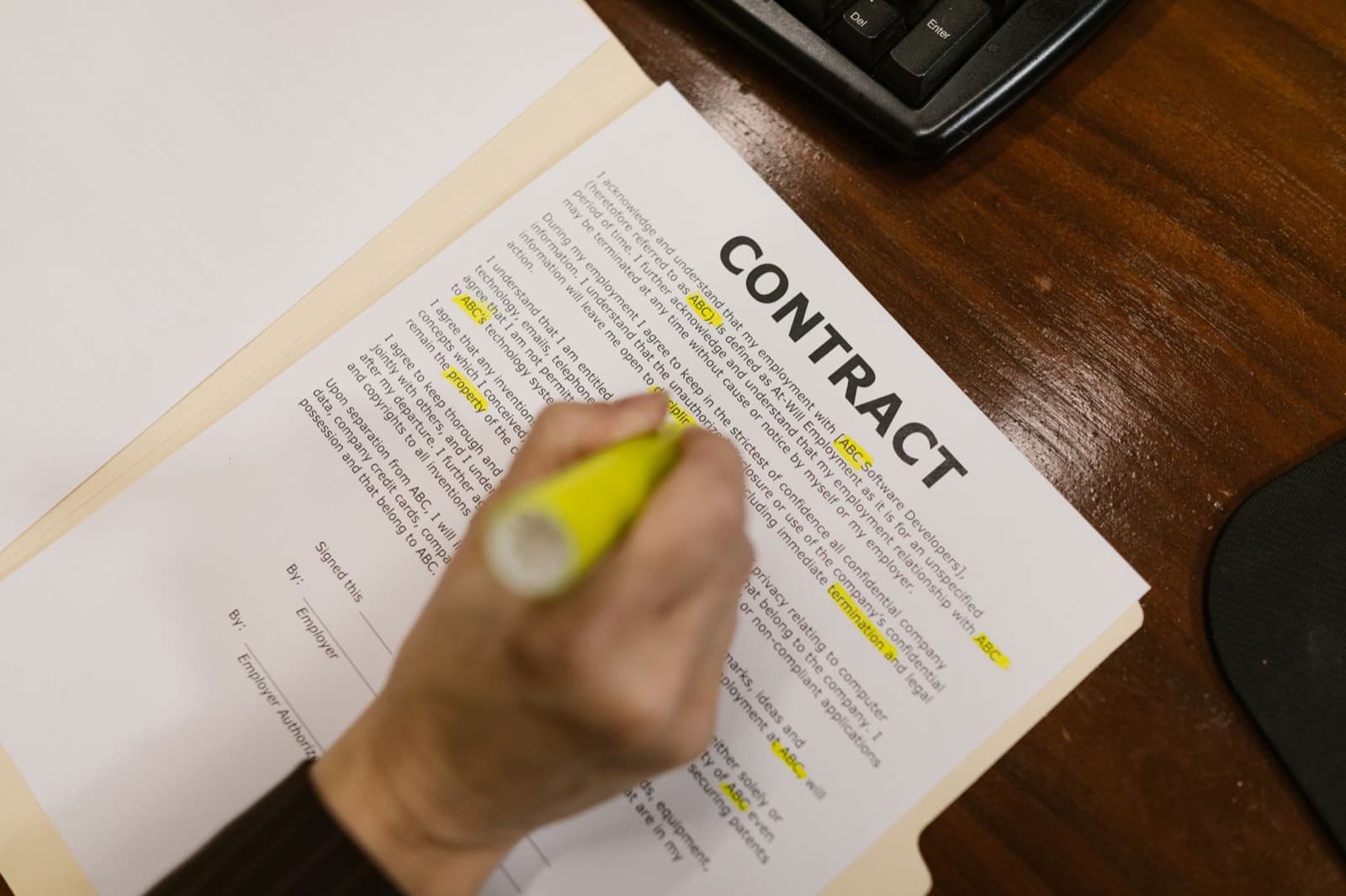 Hand marking clauses on a printed contract with a yellow highlighter at an office desk — reading the fine print of an elevator maintenance contract