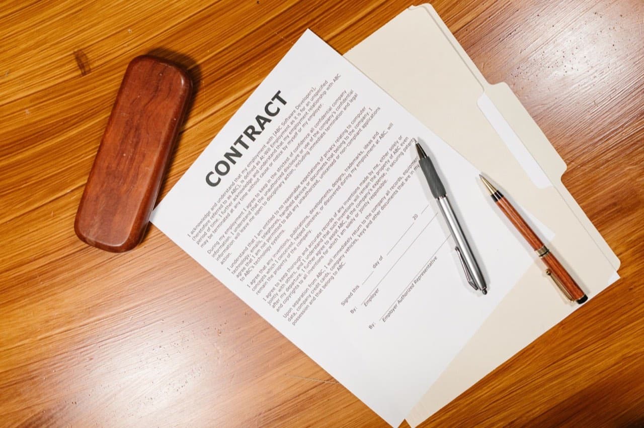 Printed contract pages and pens laid out on a wooden desk — what an elevator maintenance contract actually includes