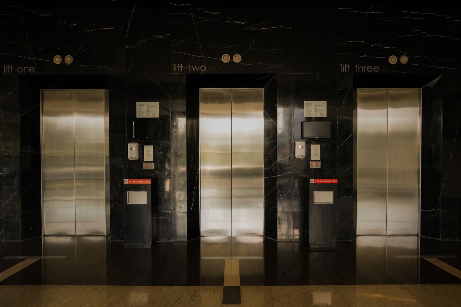 Stainless steel elevator doors in a marble lobby — weighing elevator modernization vs. replacement