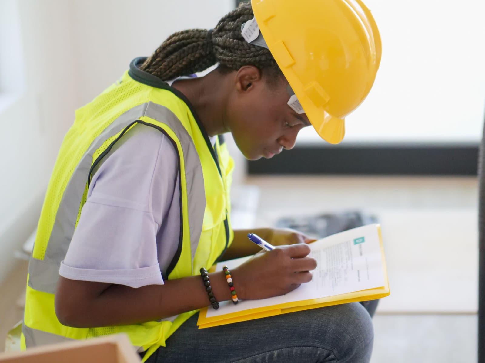 Engineer in a yellow hard hat and safety vest filling out an inspection form on a clipboard — the field work of an independent elevator consultant