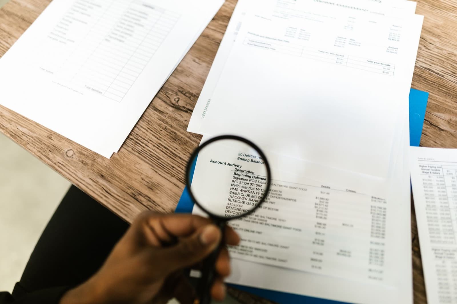 Hand holding a magnifying glass over financial statements and paperwork on a wooden desk — scrutinizing an elevator maintenance contract for red flags