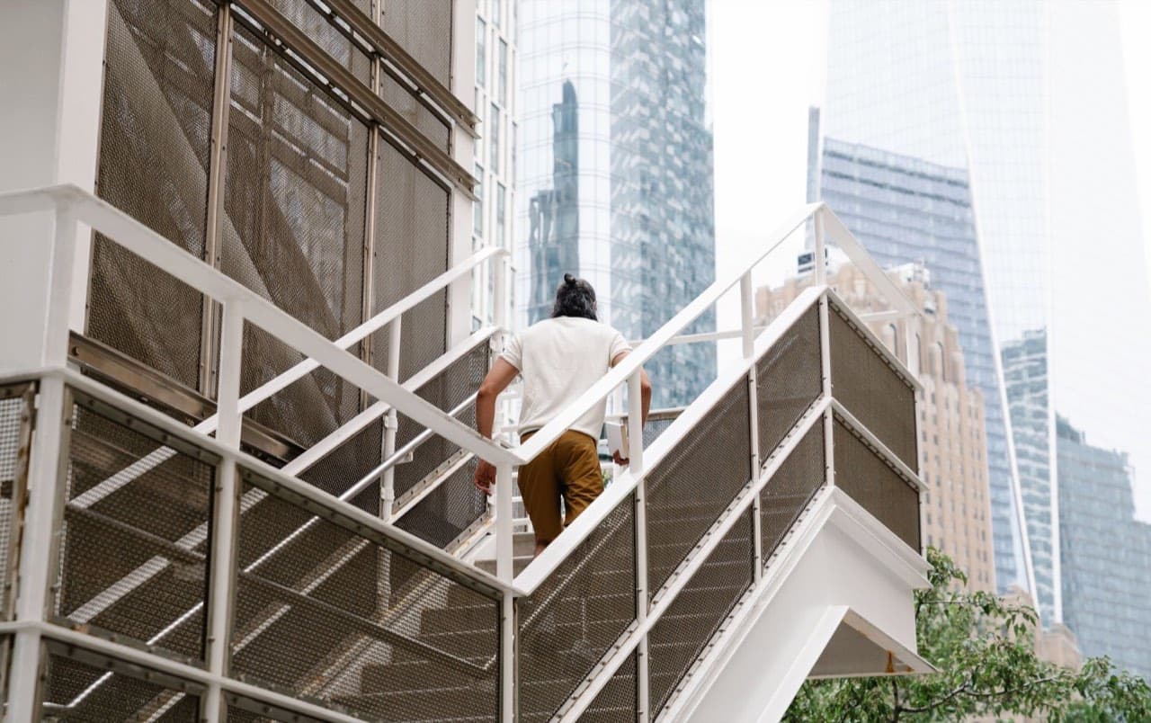 Man climbing an exterior staircase between high-rise office towers — tenants taking the stairs while an elevator is out of service
