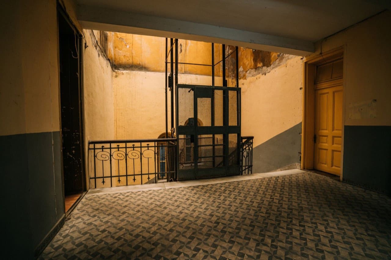 Antique cage elevator in a worn tiled hallway with peeling walls — the visible signs a building needs elevator modernization