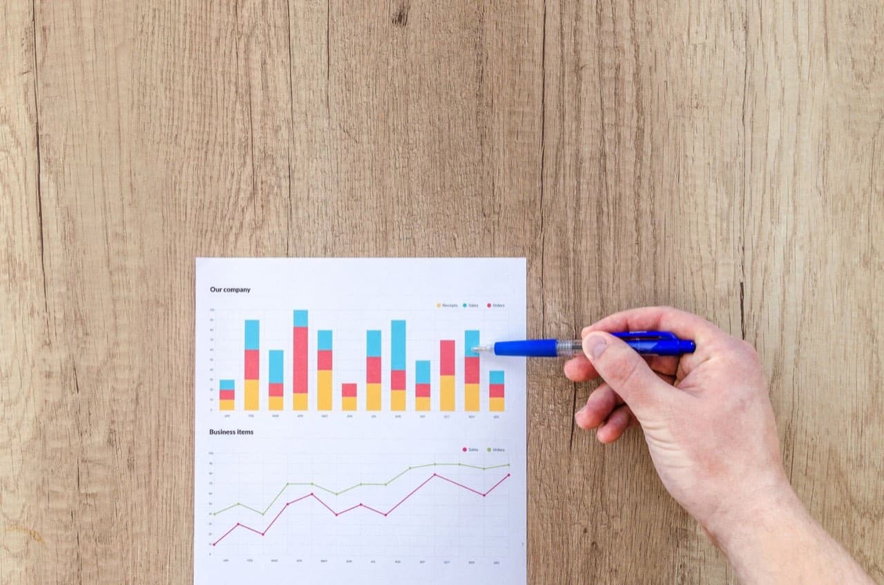 Hand pointing a pen at printed bar and line charts on a wooden table — checking quotes against elevator pricing benchmarks