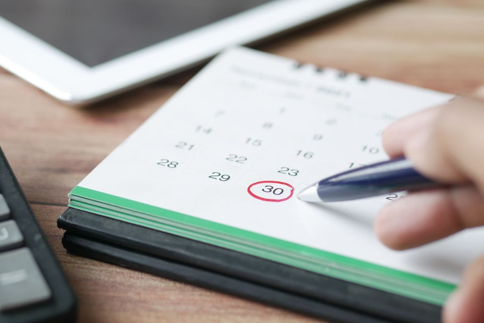 Pen circling a date on a desk calendar next to a calculator and tablet — mapping out an elevator modernization timeline